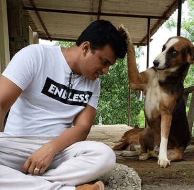 A man in a white t-shirt and a black, brown and white indie pariah dog pose