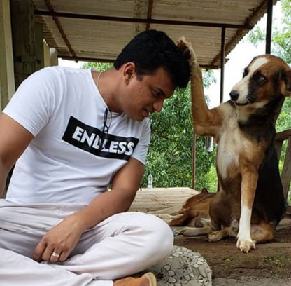 A man in a white t-shirt and a black, brown and white indie pariah dog pose