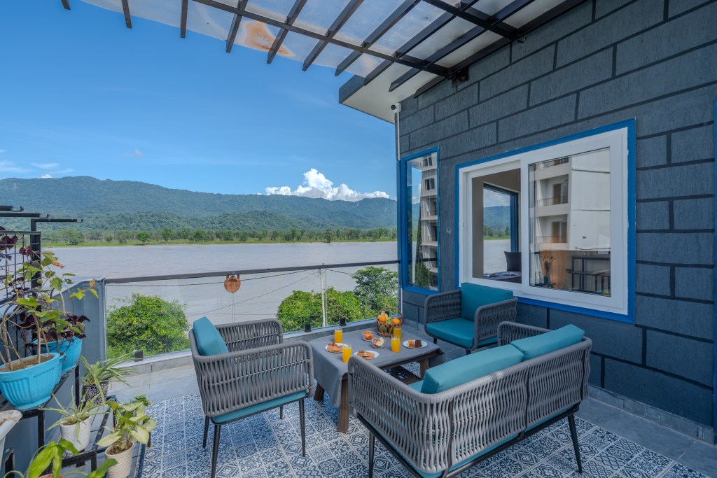 SaffronStays Tarangini by Ganges riverside villa terrace overlooking the Ganga in monsoon, Rajaji National Park forest visible. 