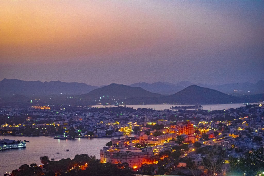 Udaipur City Palace lit up at night, viewed from a rooftop