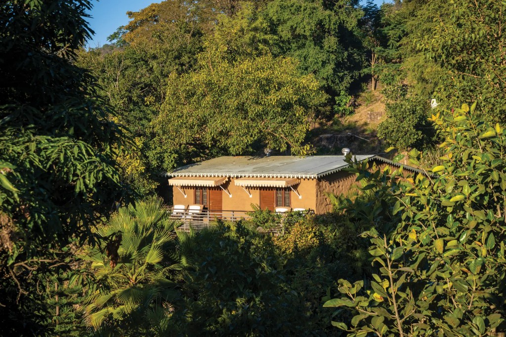 SaffronStays Sylvan Farms exterior with organic farmland and garden, misty Aravalli hills in the background