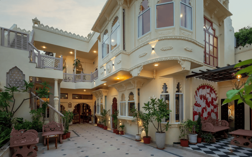 A beautiful courtyard of a traditional Indian house featuring intricate architectural details, lush greenery, and well-maintained plants.