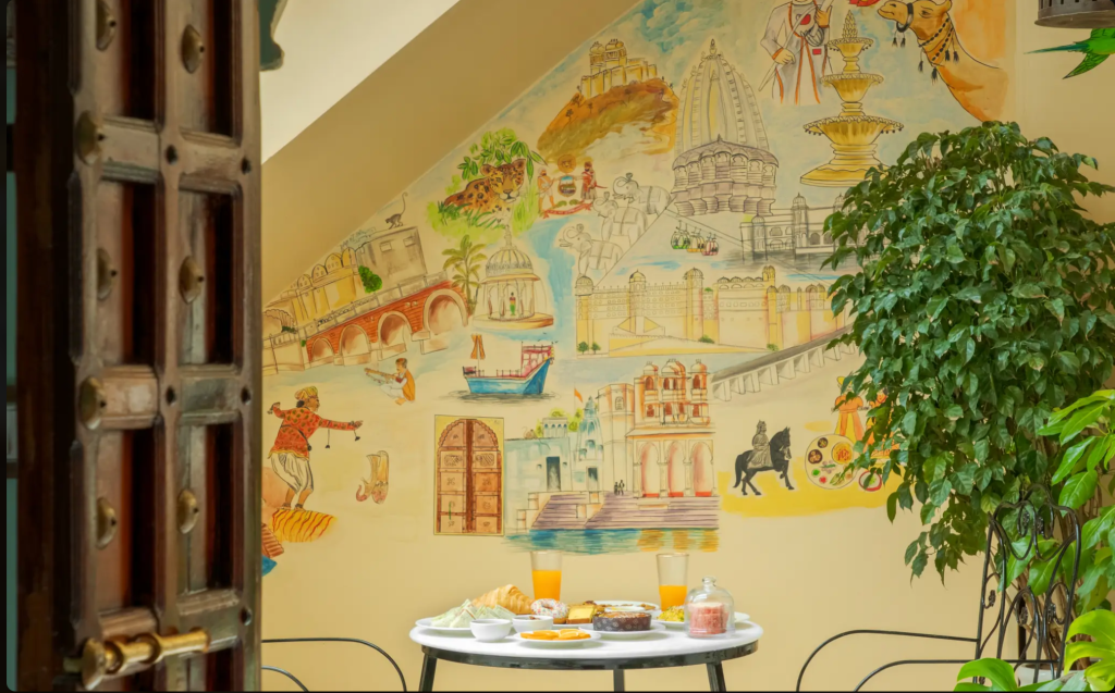 A cozy dining setup with a white table displaying various dishes and drinks, surrounded by a decorative mural featuring cultural landmarks and scenes.