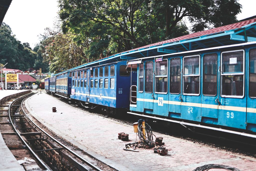 Blue vintage train cars parked at a railway station surrounded by greenery.
