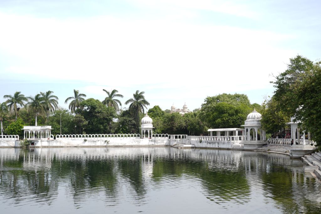 A serene lake surrounded by lush greenery and palm trees, featuring white ornate structures along the bank.