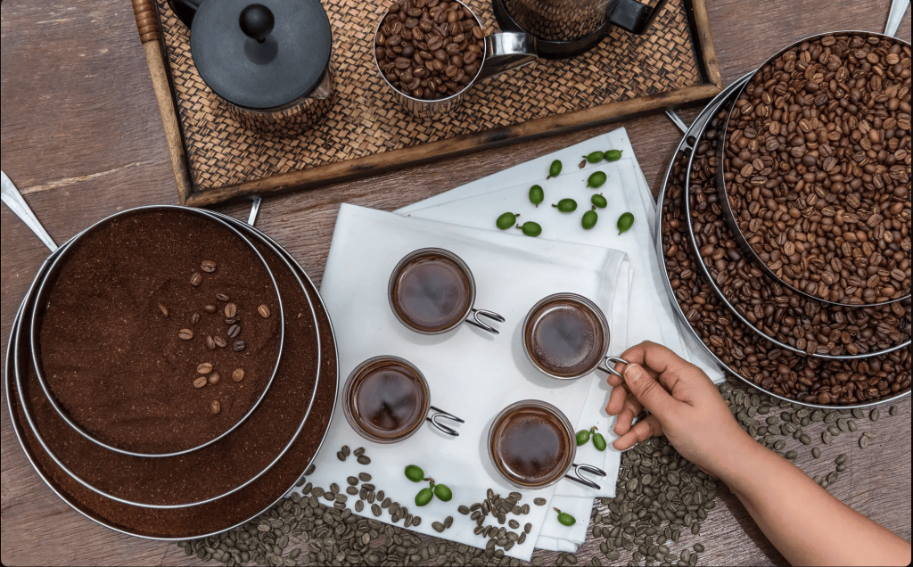 An assortment of coffee products including ground coffee, whole coffee beans, and cups of brewed coffee, arranged on a wooden table.