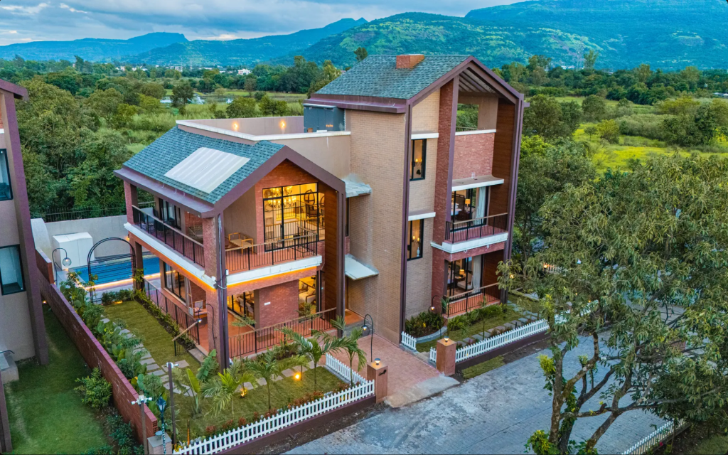 Aerial view of a modern three-story building surrounded by greenery, featuring balconies and a swimming pool area.
