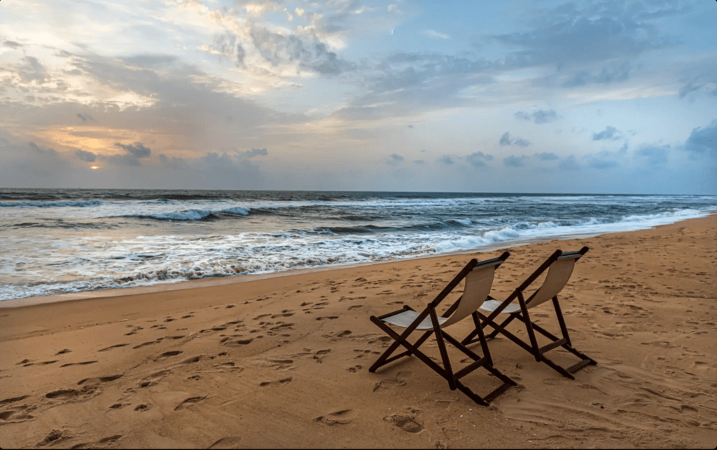 Two beach chairs facing the ocean on a sandy beach during sunset with gentle waves.