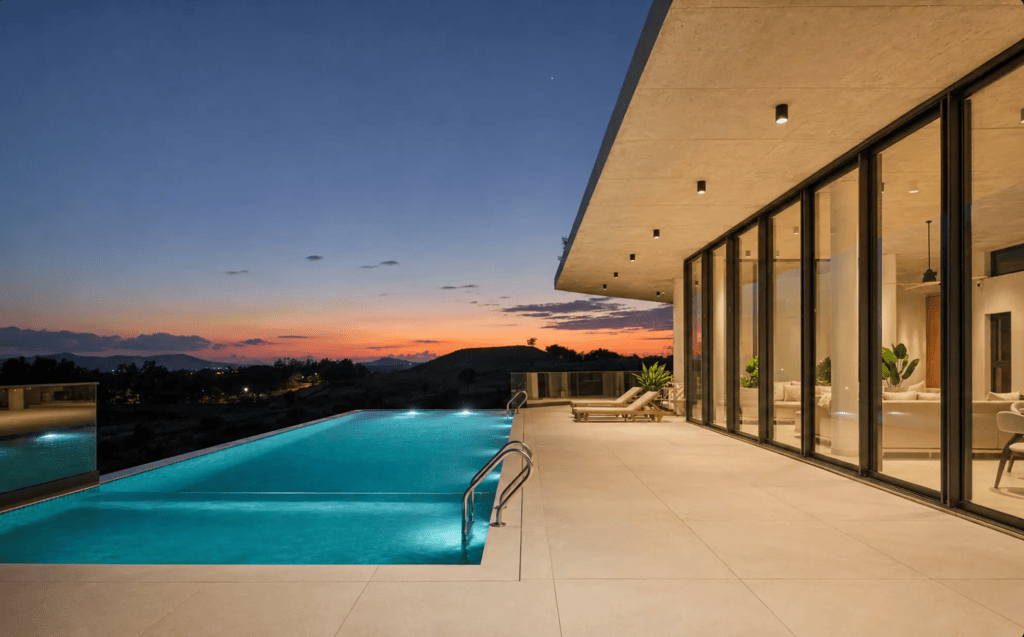 Contemporary home exterior with a spacious terrace and infinity pool at dusk, showcasing a vibrant sunset sky.