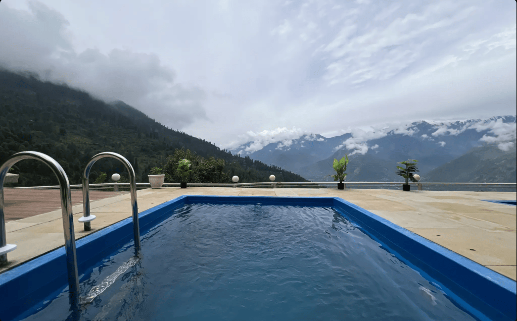 Outdoor swimming pool with a view of misty mountains and cloudy sky.