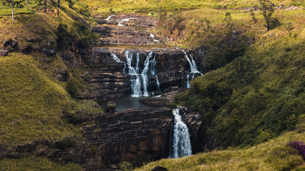 A scenic view of cascading waterfalls surrounded by lush green hills and rock formations.