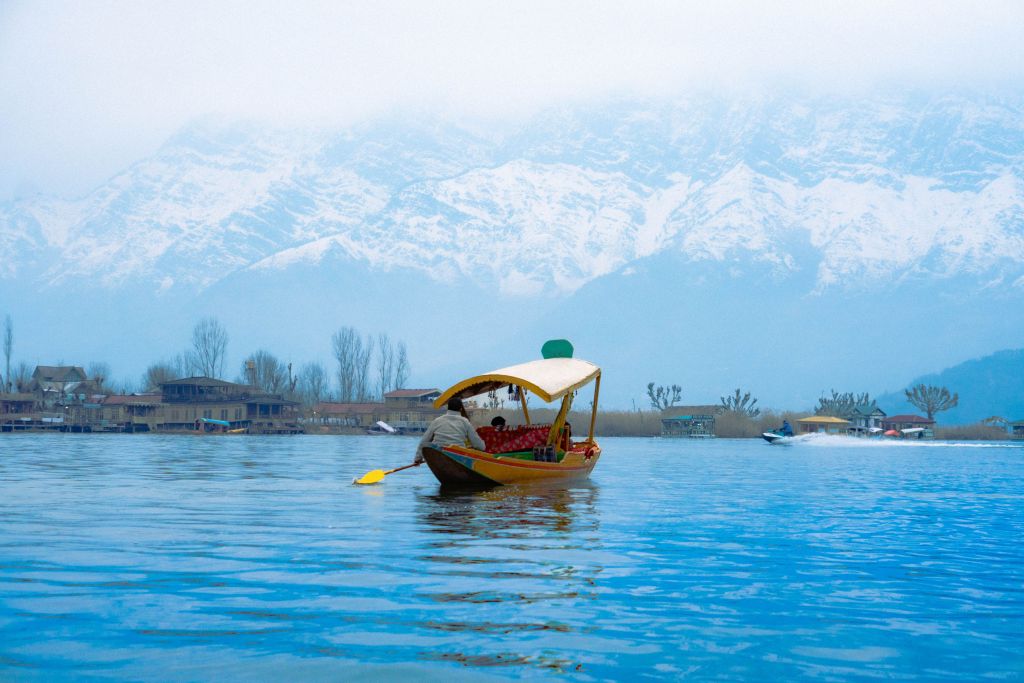 A traditional wooden boat gliding across a serene lake, with snow-capped mountains in the background and mist hovering over the water.