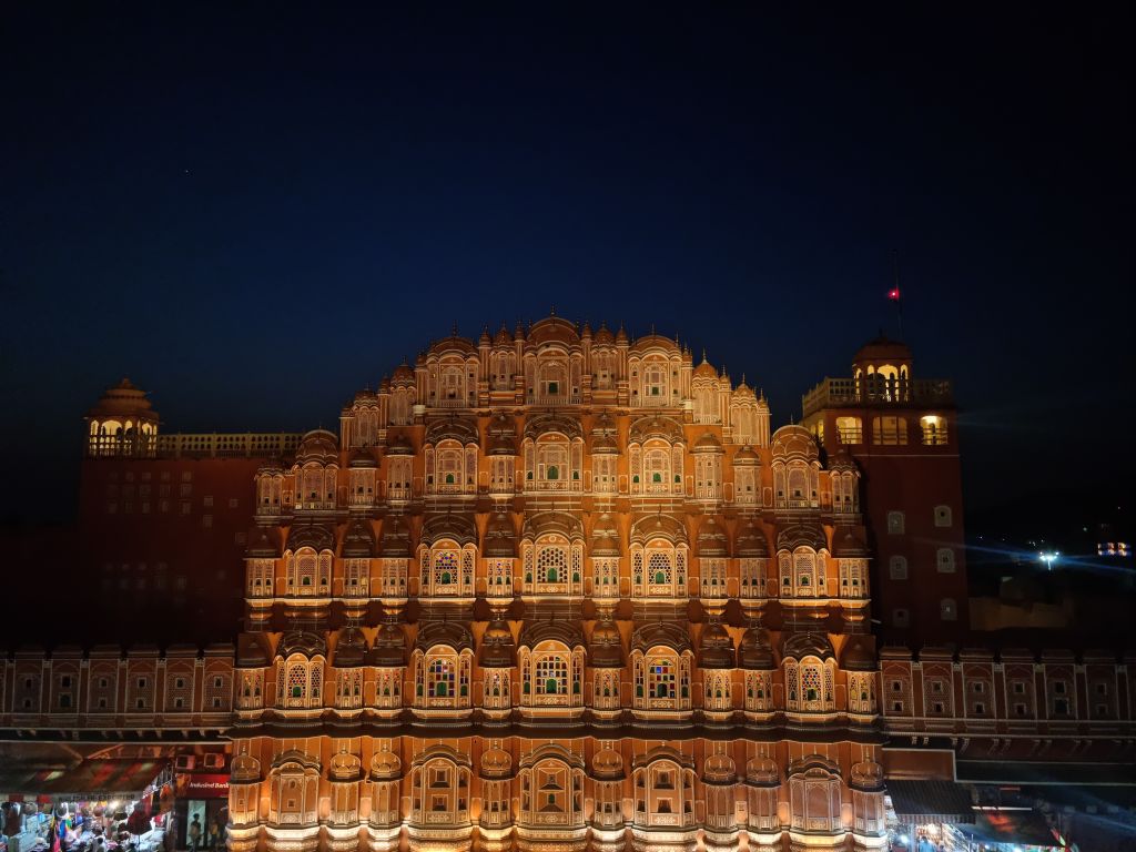 A night view of the Hawa Mahal, also known as the Palace of Winds, showcasing its intricate architecture and colorful windows against a dark sky.