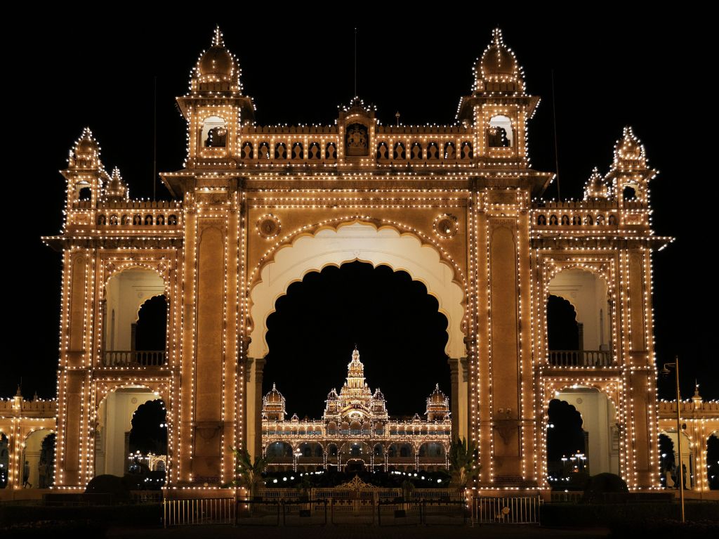 A beautifully illuminated architectural archway at night, showcasing intricate designs and decorative lights, with a grand building visible in the background.